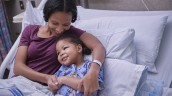 Parent comforting smilingchild in hospital bed