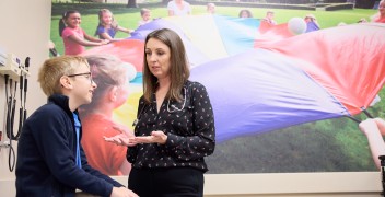 Physician talks to child sitting in clinial room, a picture of children playing outside appears on the wall