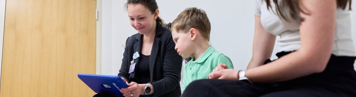 clinician looking at handheld device sitting next to patient and family