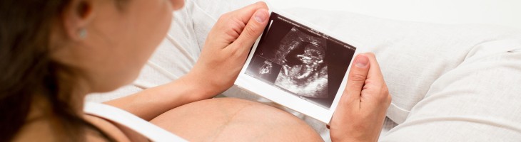 Pregnant woman sitting down looking at an ultrasound photo