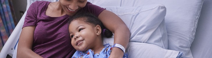 Parent comforting smilingchild in hospital bed