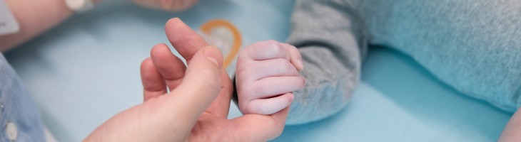 hands grapsing infant laying in bed