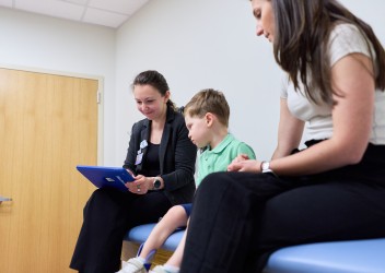 clinician looking at handheld device sitting next to patient and family