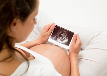 Pregnant woman sitting down looking at an ultrasound photo