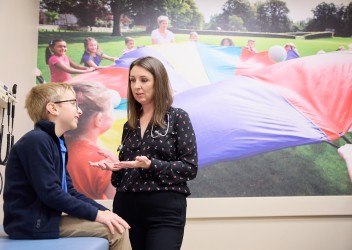 Physician talks to child sitting in clinial room, a picture of children playing outside appears on the wall