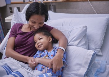Parent comforting smilingchild in hospital bed